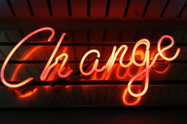 A reddish orange neon sign that reads Change in cursive font appears against a dark background