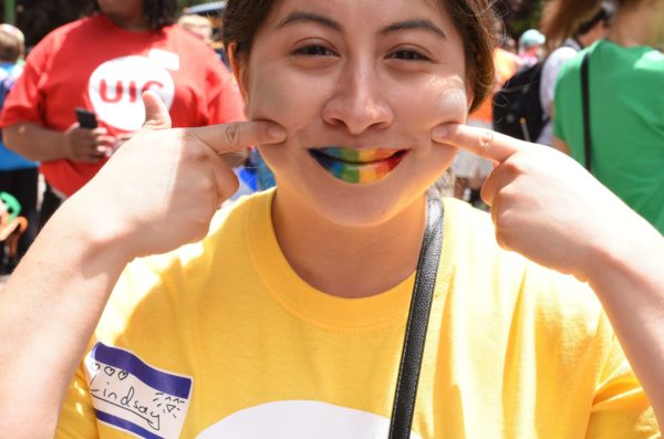 Student wearing rainbow lipstick pointing to their smiling lips and wearing a UIC t shirt.