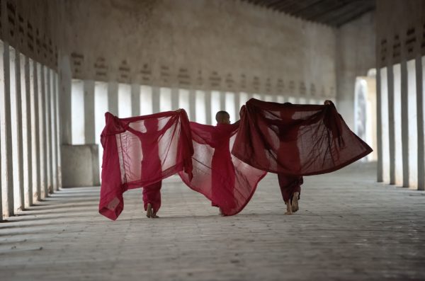 Women with large red scarves holding them up and looking through them.