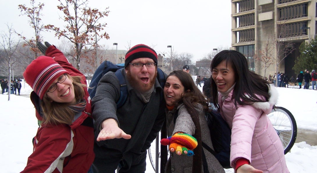 Four people stand together outside with palms outstretched.