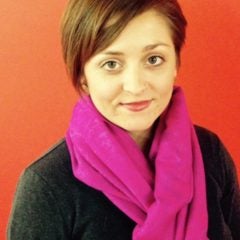 In this headshot, Dr. Jennifer S. Ash smiles at the camera, wearing a long sleeve black shirt and bright pink scarf.