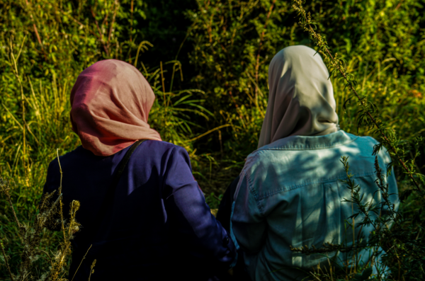 Two people in hijabs sit outside, facing away from the camera.