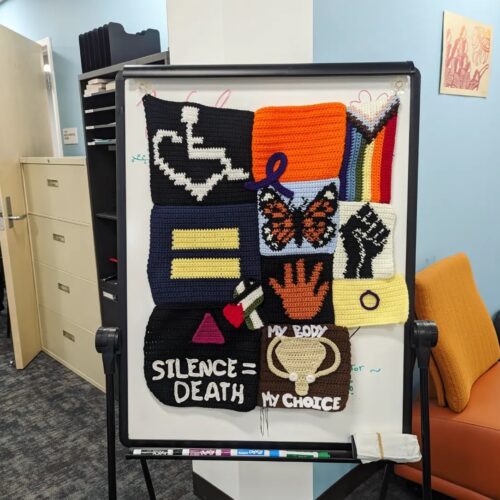 Social Justice in the Eye of Crochet, a crochet piece by GWS major Bri Saldana, is displayed on a white easel.