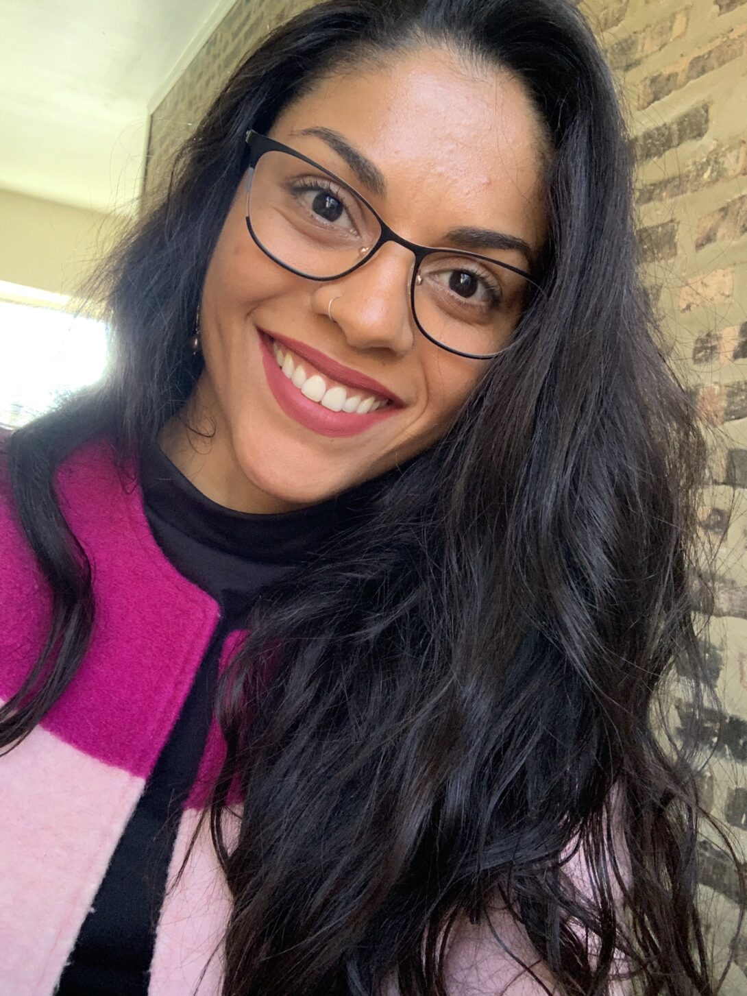 A person with glasses and black hair is centered in this selfie, with a brick wall in the background.