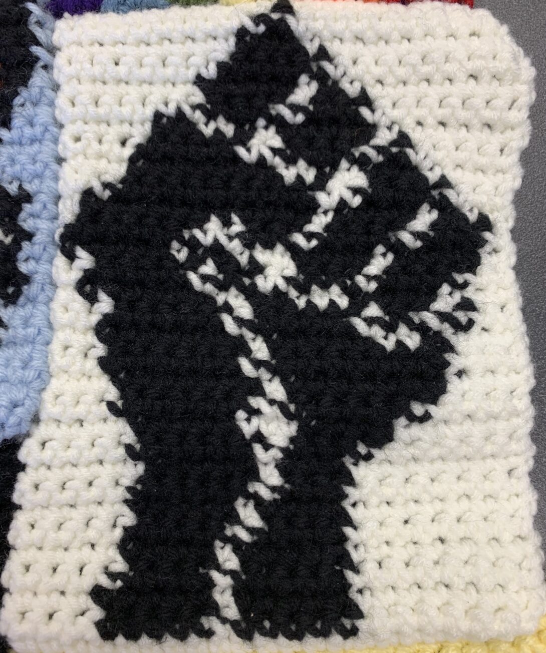 A black fist with white outlines is crocheted in the center of a white crochet square