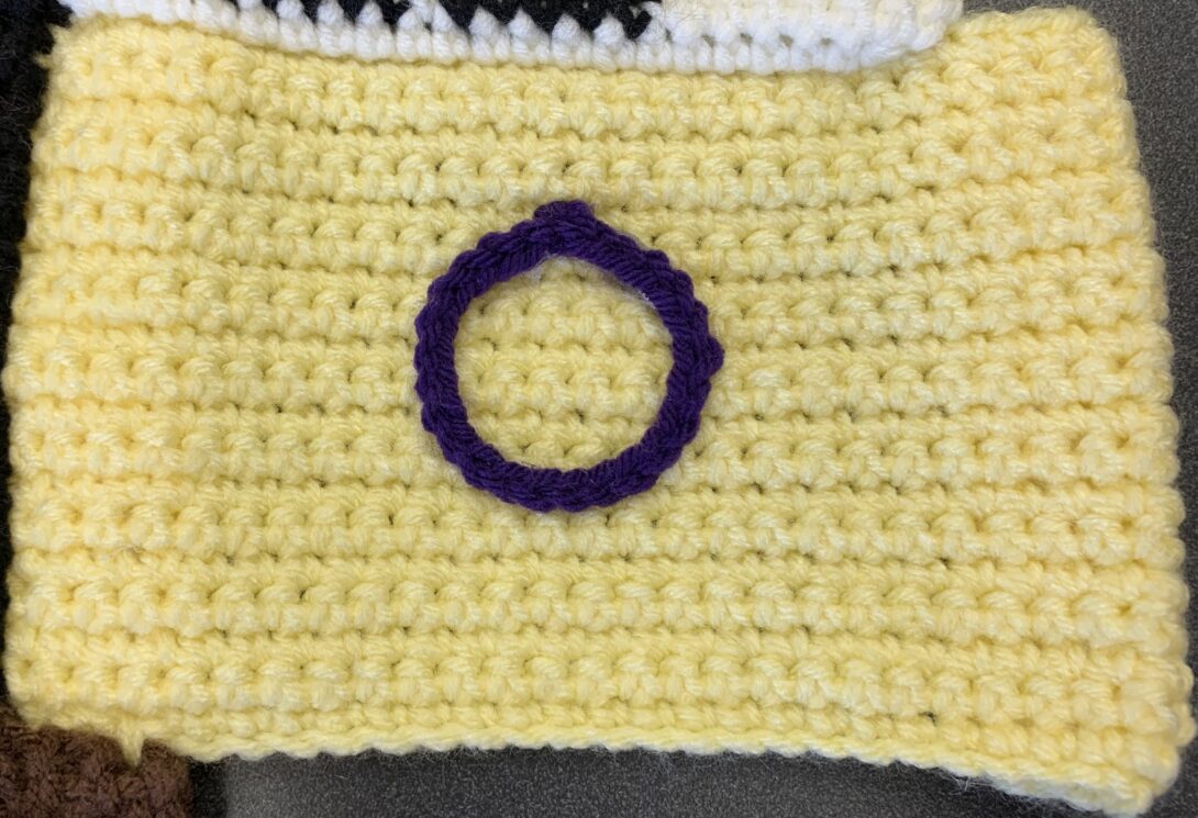 A purple crocheted outline of a circle appears in the center of a yellow crocheted background